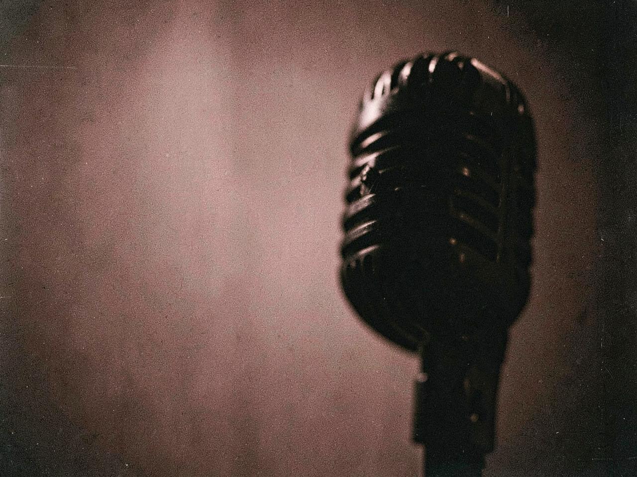 A vintage broadcast microphone in deep shadow against a dusty rose backdrop